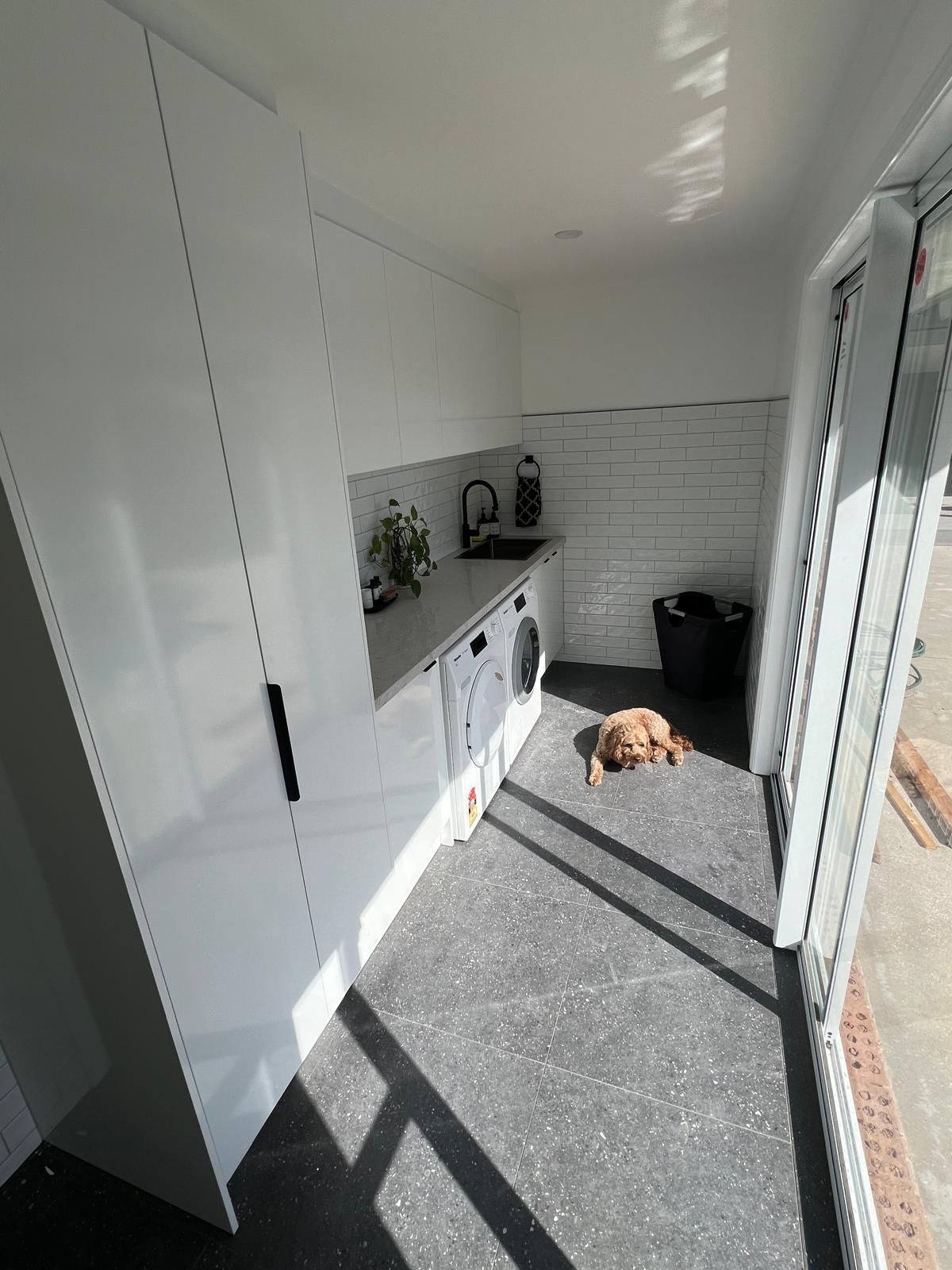 Renovated laundry with white cabinetry, subway tiles and stone floor